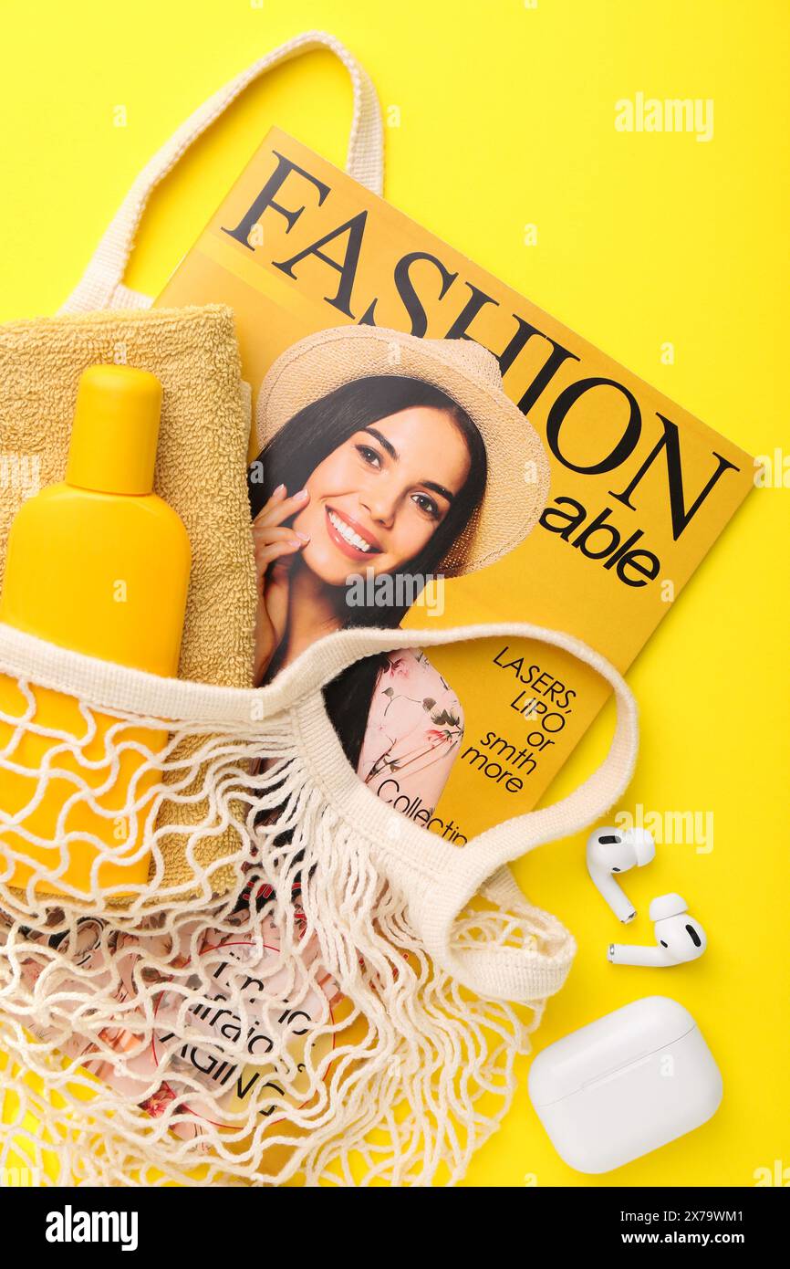 Borsa a cordoncino con rivista di moda e accessori da spiaggia su sfondo giallo, piatto Foto Stock