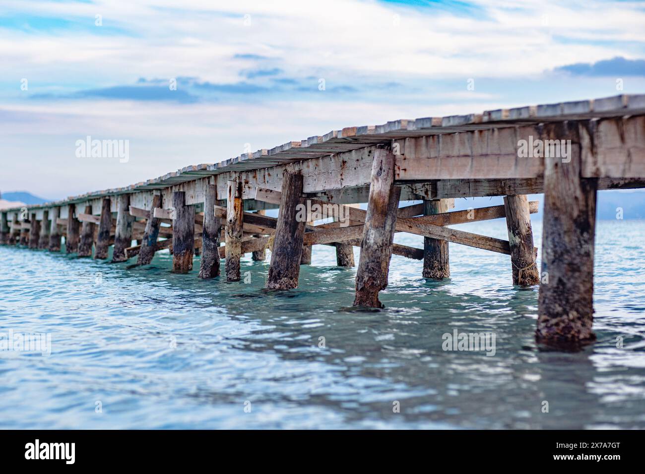 Foto di un molo di legno che si estende fino al mare. Bella vista laterale del molo. Calme acque turchesi, struttura a ponte in legno e cielo meraviglioso. Foto Stock