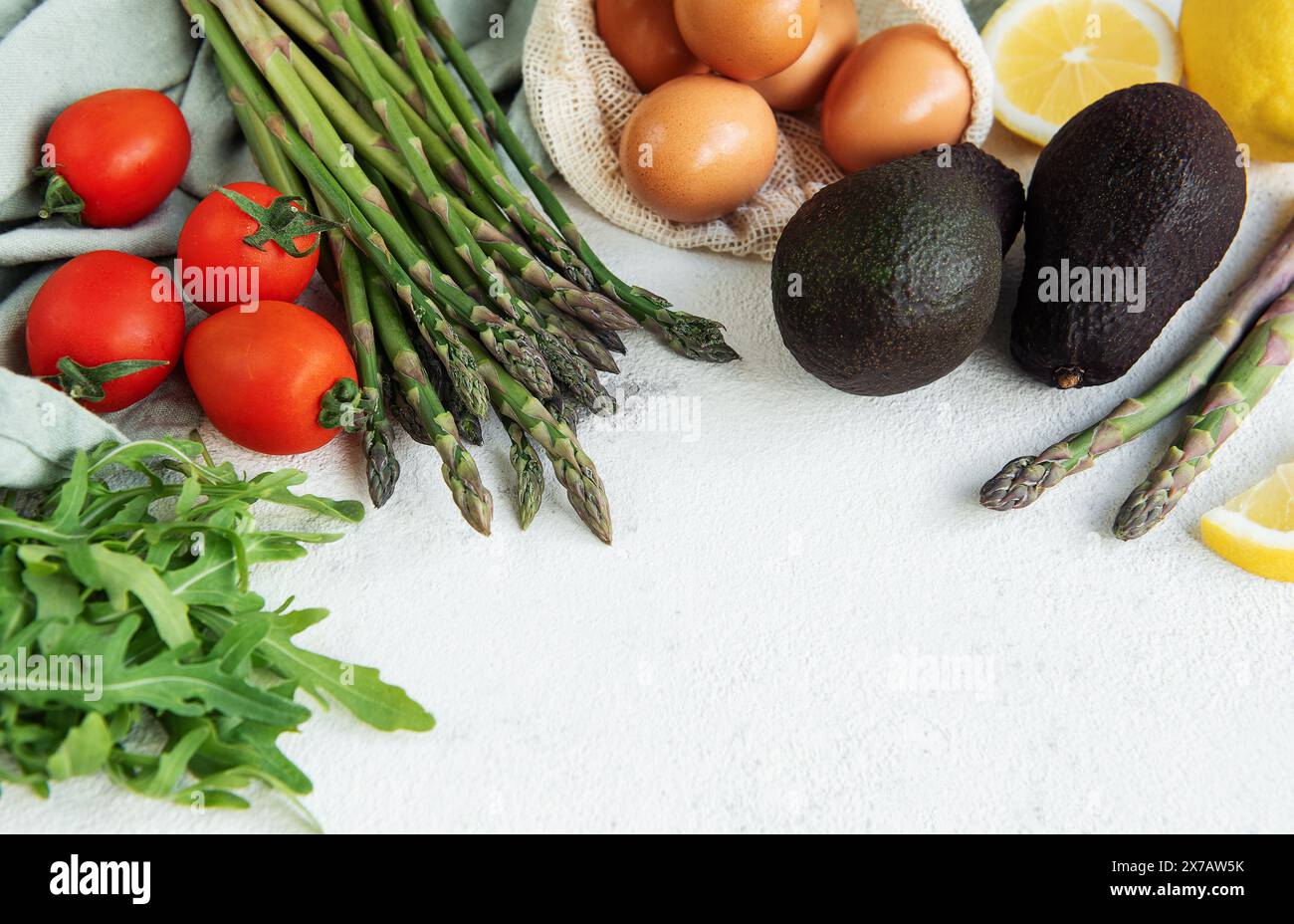 Una varietà di verdure fresche, tra cui asparagi, pomodori e rucola, sono ordinatamente organizzati accanto a avocado maturi e un sacchetto di uova scure. L'arr Foto Stock