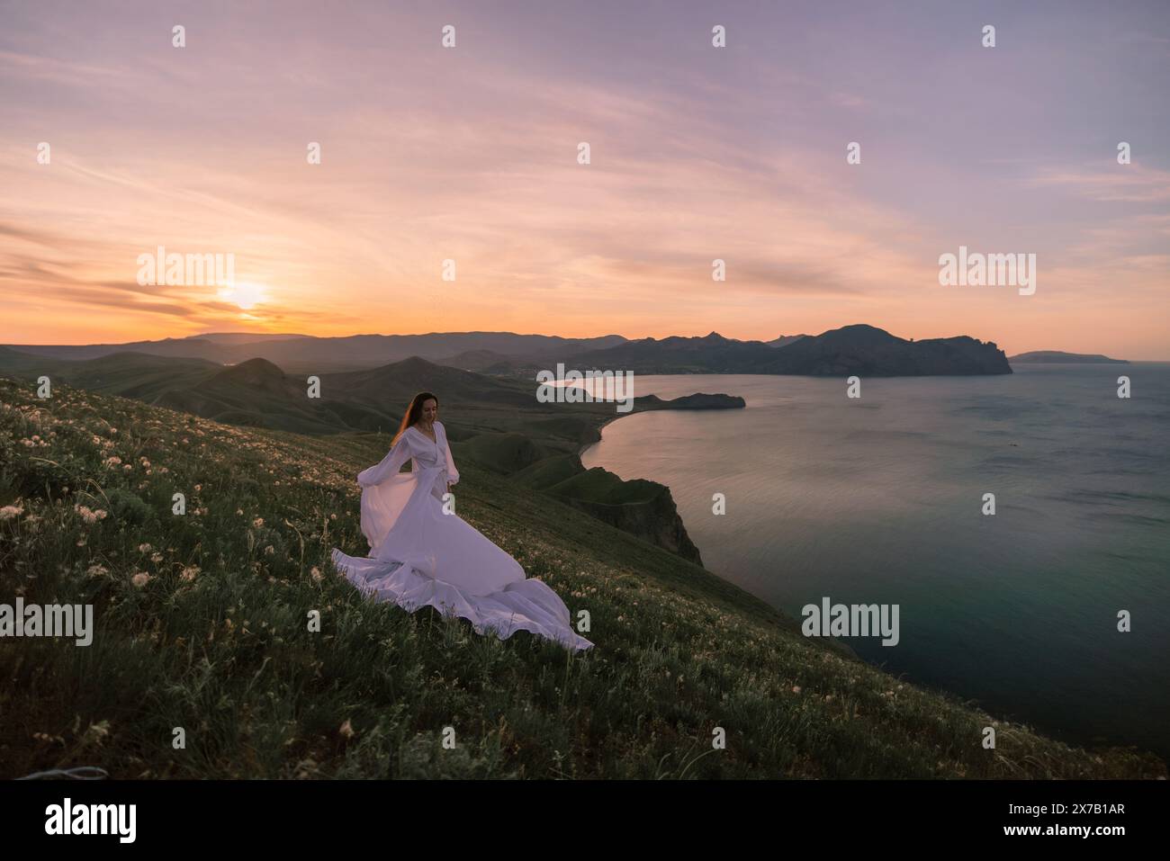 Una donna con un abito bianco si trova su una collina che domina un corpo d'acqua Foto Stock