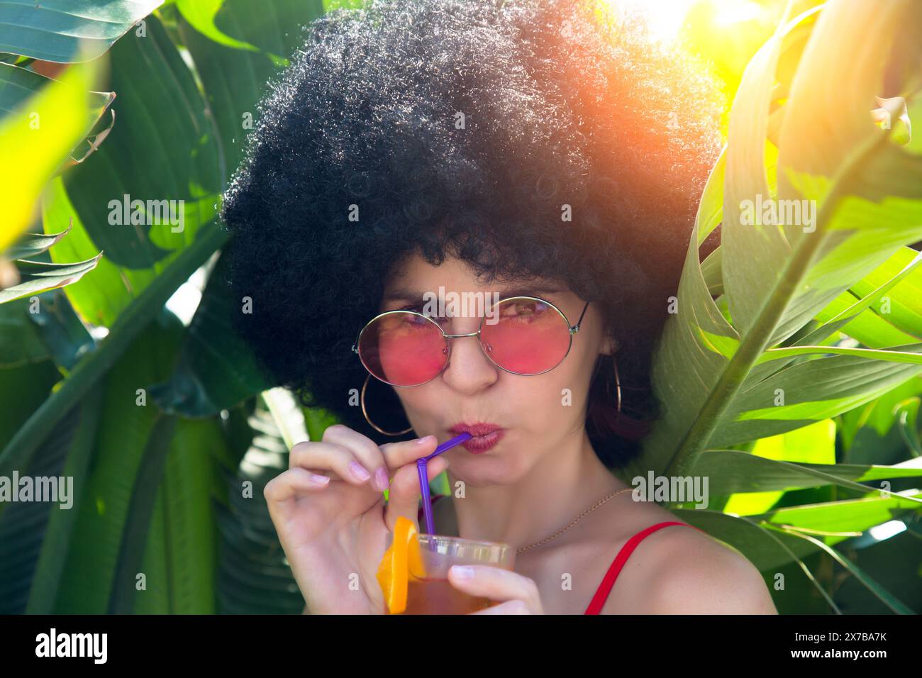 donna in una fitta vegetazione che beve cocktail alcolici con occhiali da sole. Foto Stock