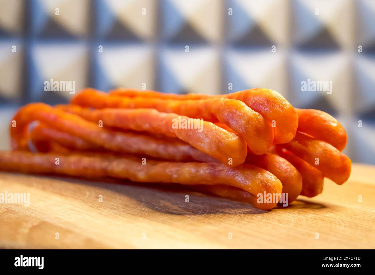 Una pila di salsicce su una tavola di legno, con sfondo piastrellato blu e bianco. L'immagine è luminosa e adatta per pubblicità di cibo o cibo Foto Stock