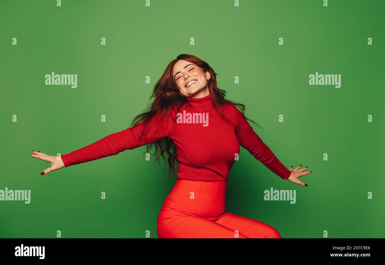 Giovane donna felice in un abbigliamento casual si siede su uno sfondo verde, irresistibile di gioia e libertà. Foto Stock