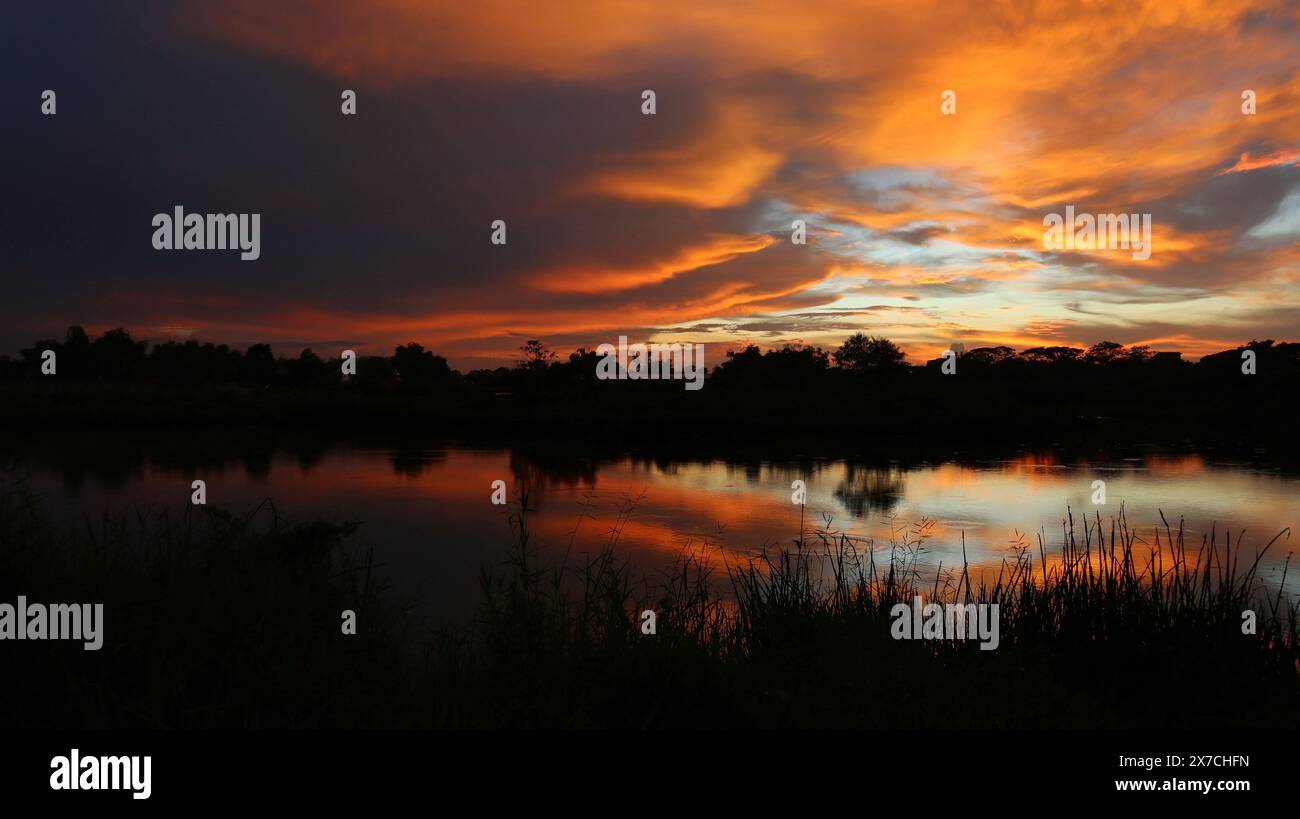 Esotico cielo nuvoloso arancione al tramonto con riflessi nell'acqua del lago Foto Stock