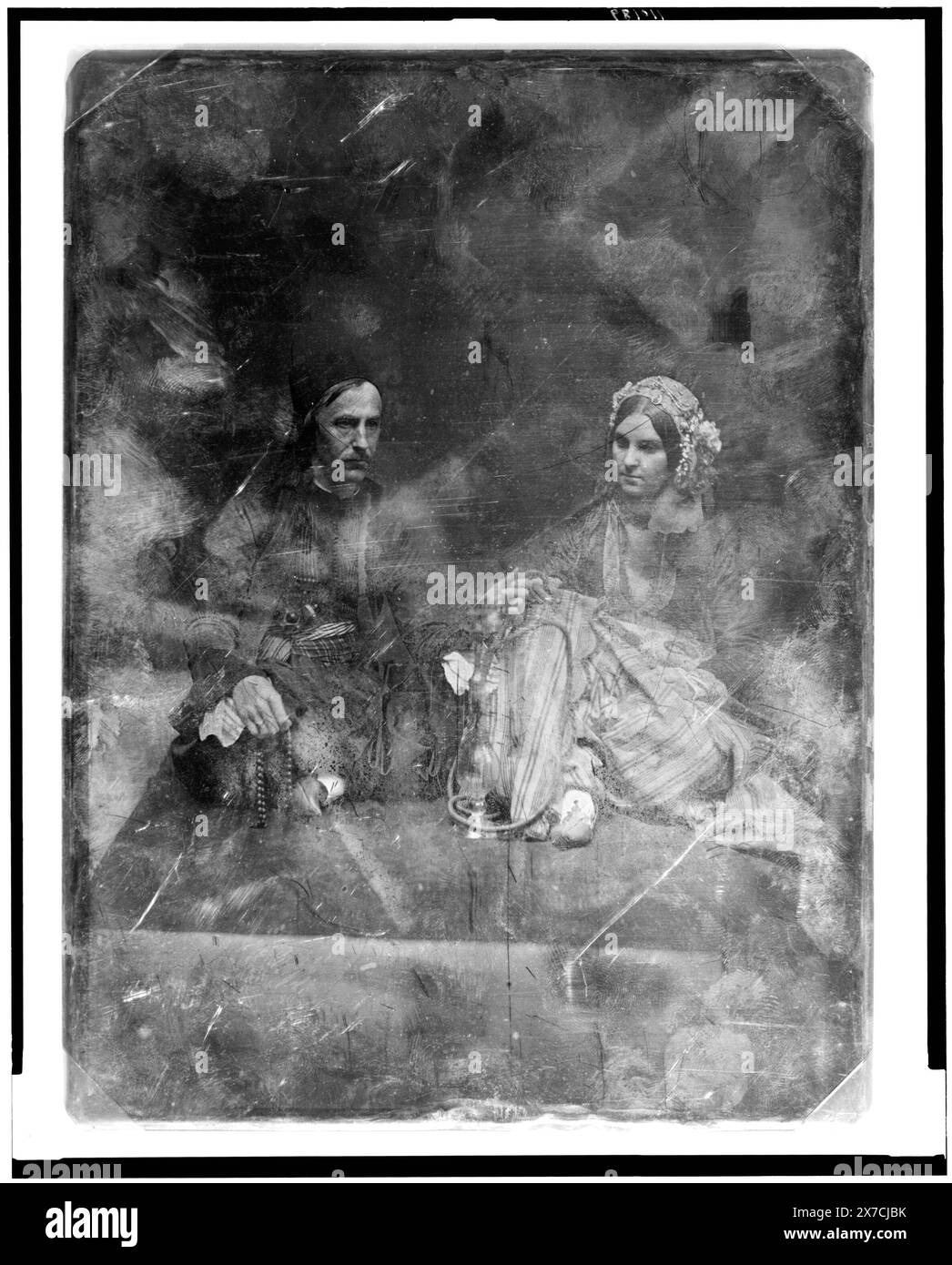Uomo non identificato, di circa 40 anni e una donna un po' più giovane, entrambi in costume orientale, ritratti a figura intera, entrambi seduti su un tappeto sul pavimento, l'uomo, a sinistra, a gambe incrociate, girò tre quarti a destra, tenendo una stringa di perline; la donna girò leggermente a sinistra, indossando un berretto con perline; tra di loro c'è un narghilè, il cui gambo sono entrambi in mano, Corners trimmed., Hallmark: Rinhart 29., scritto sul retro del piatto: 507(X)., Transfer; U.S. War College; 1920; (DLC/PP-1920:46153)., fa parte di: Daguerreotype Collection , prodotta dallo studio di Mathew Brady. Foto Stock