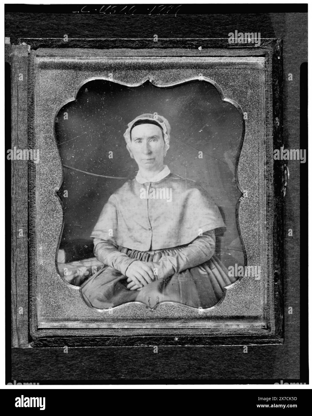 Donna non identificata, ritratto di tre quarti di lunghezza, rivolta verso la parte anteriore, seduta su una sedia accanto al tavolo con tovaglia; libro sul tavolo, fotografo non identificato., può essere copia daguerreoype., Hallmark: Possibilmente Rinhart 46., cassa: Anteriore, fiori misti; retro, quadrafoil., source unknown., fa parte di: daguerreotype Collection , . Foto Stock