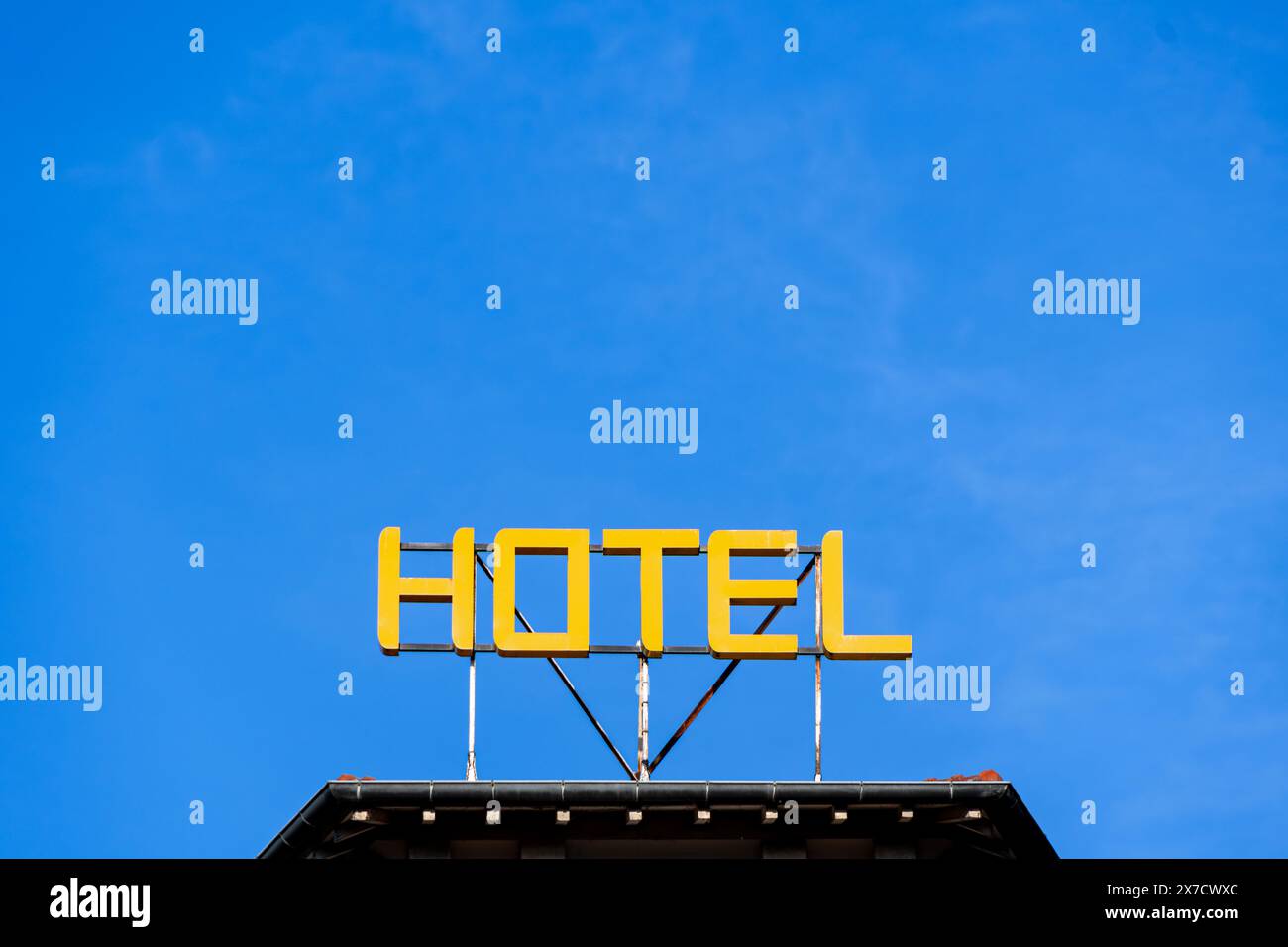 Cartello con la parola "HOTEL" scritta in lettere maiuscole gialle luminose sul tetto di un edificio su uno sfondo blu del cielo. Spazio negativo Foto Stock