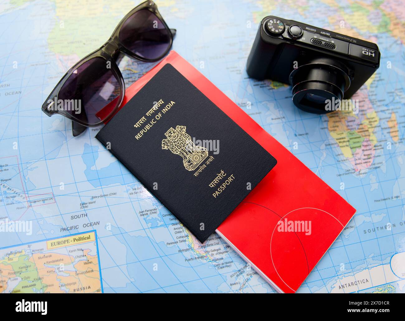 Esplora il mondo con questo piatto essenziale da viaggio con passaporto indiano, occhiali da sole e una macchina fotografica che si trova su una mappa del mondo d'epoca. Foto Stock