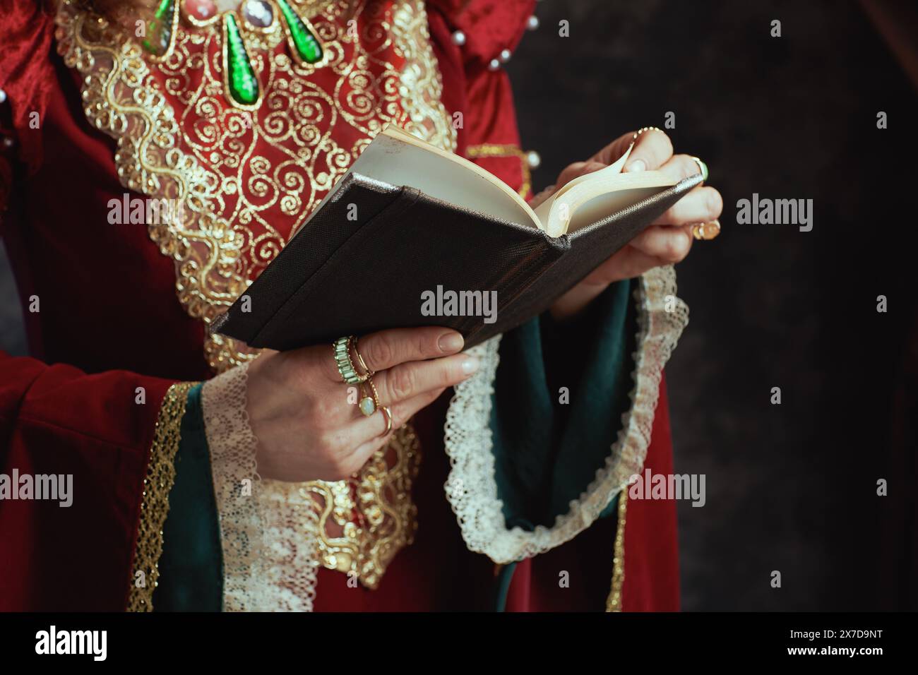 Primo piano sulla regina medievale in abito rosso con libro su sfondo grigio scuro. Foto Stock