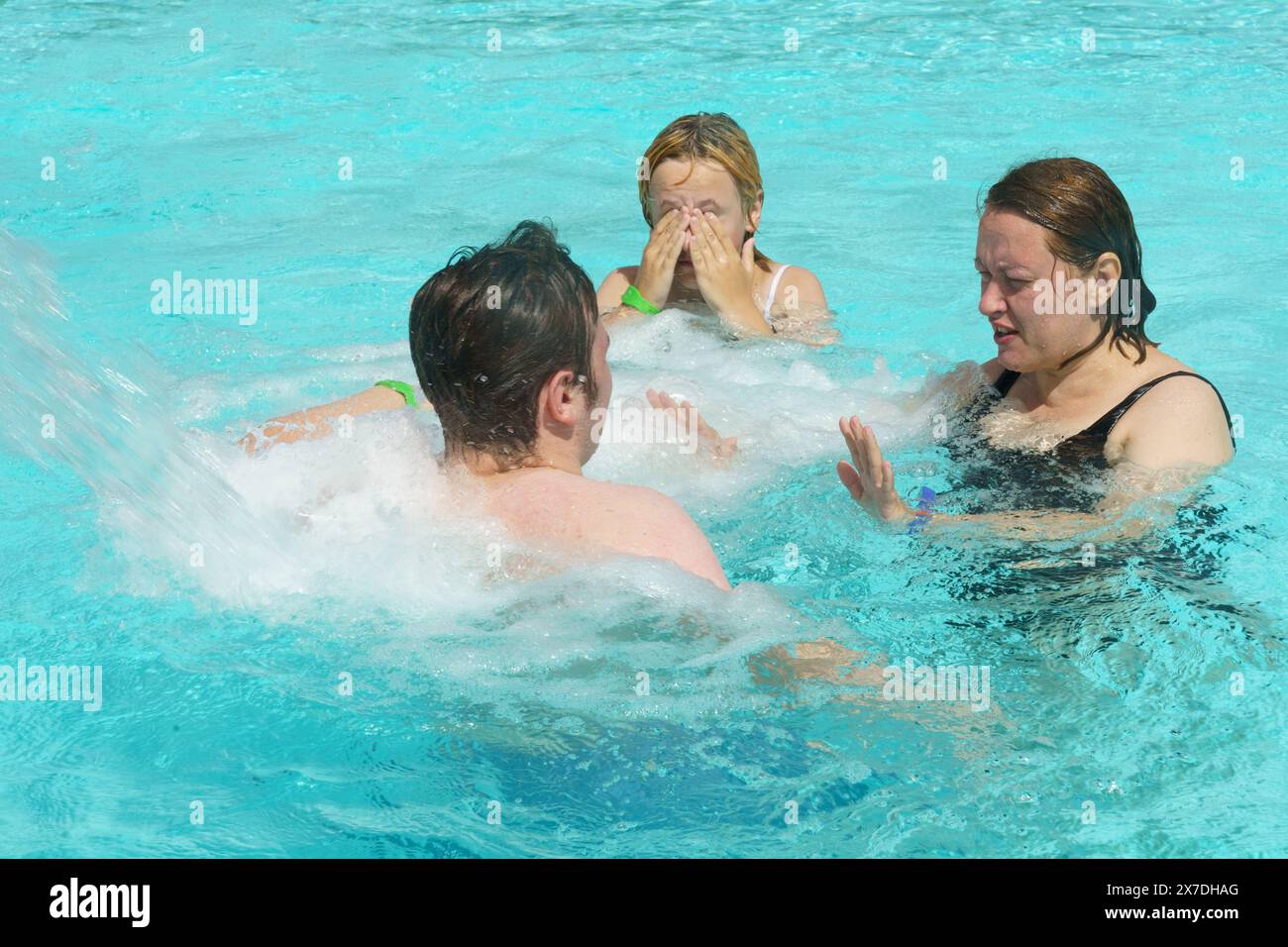 Un gruppo di individui, probabilmente una famiglia, si impegnano in attività ludiche in una piscina, godendosi l'acqua e magari utilizzando l'idromassaggio fe Foto Stock