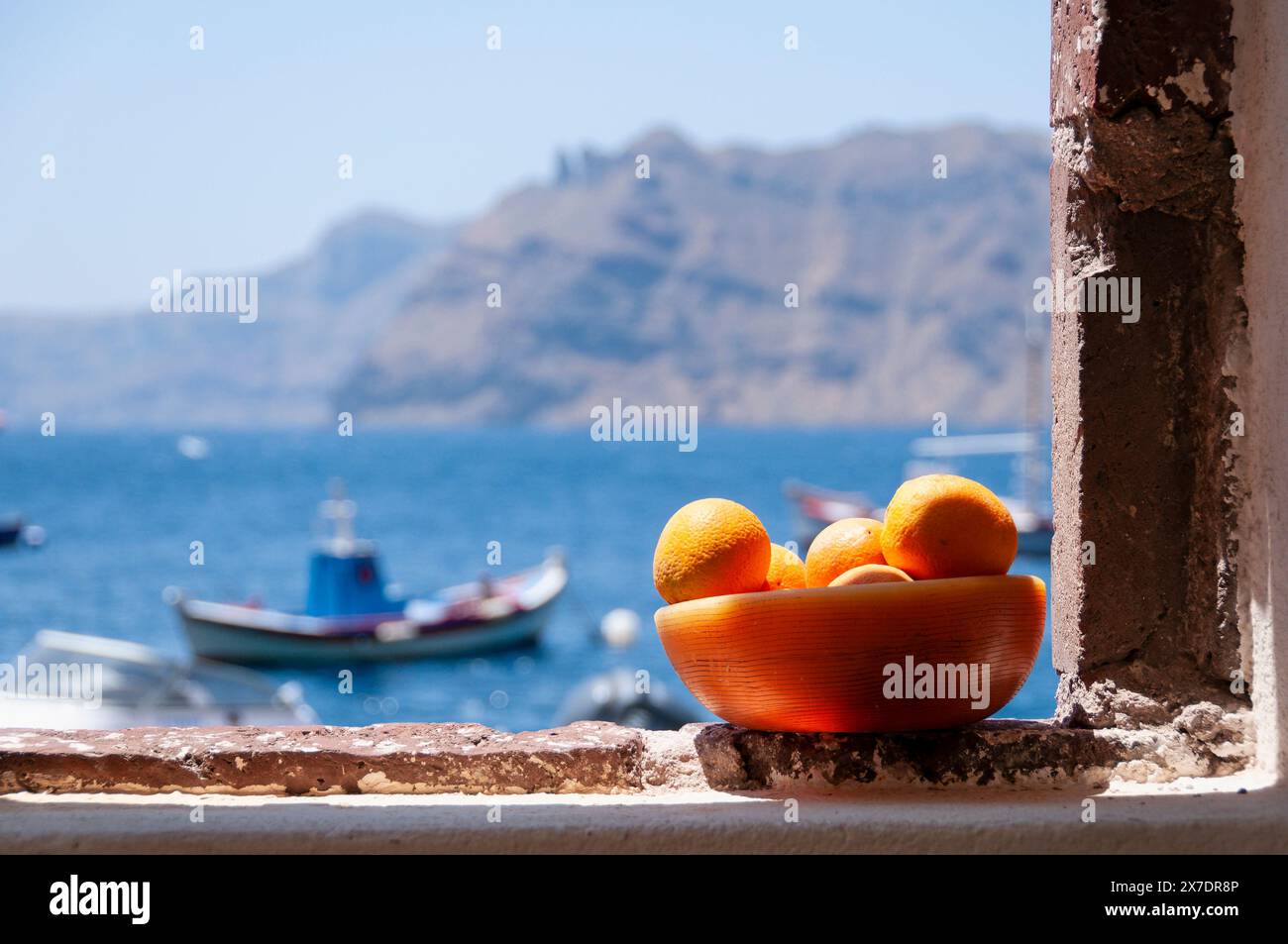 Primo piano di una ciotola di arance succose sulla finestra con una vista panoramica della caldera sull'isola di santorini in Grecia Foto Stock