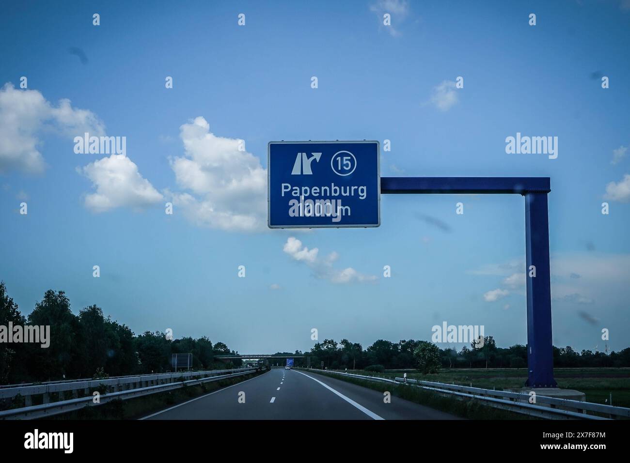 Autobahn, Straßenschild, Papenburg, 1000 m, Autobahnausfahrt, Ausfahrt 15, blauer Himmel, Wolken, Auto, Fahrbahn, Leitplanke, Bäume, Deutschland, Verkehr, Sommer, Kilometerangabe, Wegweiser, Autobahn A31, Emslandautobahn, Nord-Süd-Verbindung, Schnellstraße, Infrastruktur, Verkehrsnetz, 241 km Länge, verbindet Emden mit Bottrop, gebaut zwischen 1967 und 2004, wichtige Route für Urlauber, führt durch Niedersachsen und Nordrhein-Westfalen, landschaftlich reizvoll, wenig befahren, ermöglicht schnelle Verbindungen, geringe Verkehrsbelastung, Wichtige Verbindung für regionale Wirtschaft, erleichtert Foto Stock