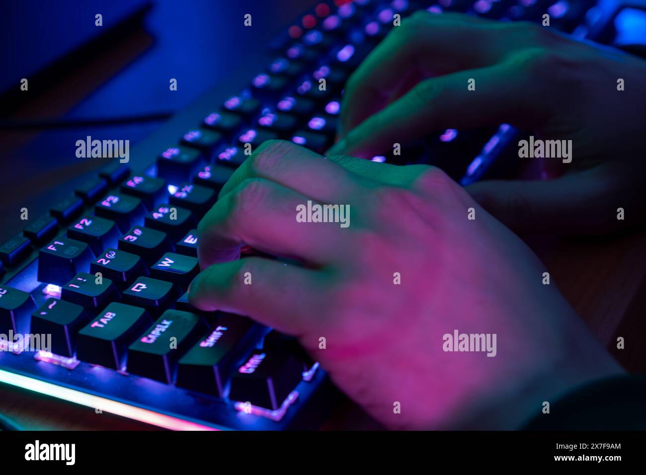 Close-up sul giocatore le mani su una tastiera, attivamente premendo pulsanti, giocando MMO giochi online. Lo sfondo è illuminato con luci al neon. Foto Stock