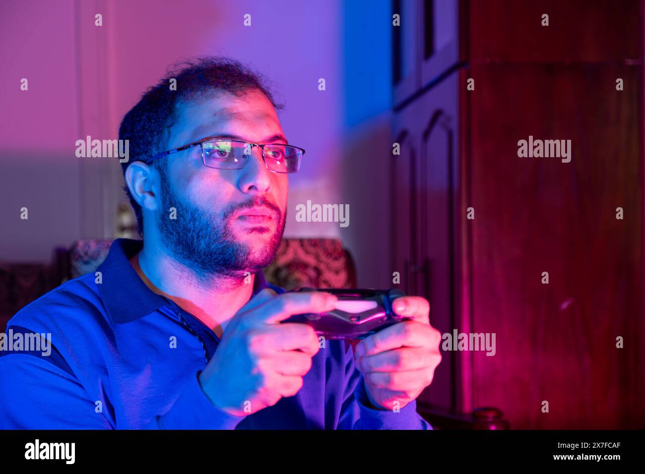 Concetto di videogame. Un ragazzo con joystick che celebra il gioco vinci, allegro uomo che solleva pugno e esclamazioni con entusiasmo, in piedi in Neon Light Over Foto Stock