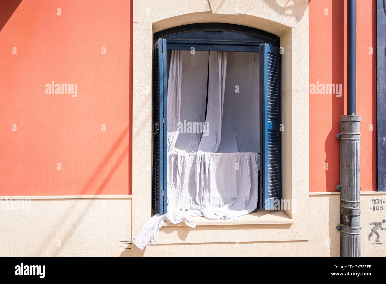 Finestra con persiane blu su un edificio con facciata bianca e rosa. Le tende bianche sono appese da una finestra di un vecchio edificio. Foto Stock