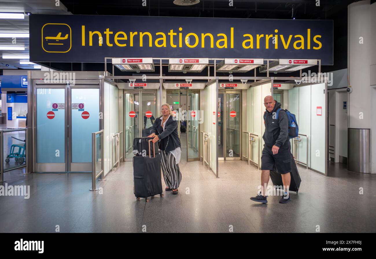 I passeggeri di sesso maschile e femminile con bagagli attraversano gli arrivi internazionali al terminal nord dell'aeroporto Gatwick di Londra, Regno Unito. Foto Stock