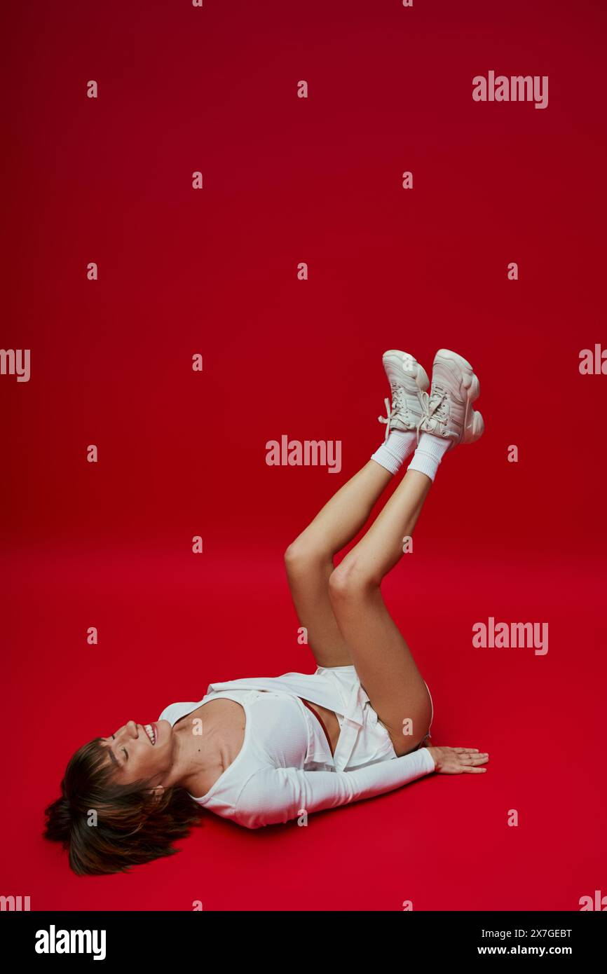 Una giovane donna in abbigliamento sportivo bianco sdraiata sulla schiena su un vivace sfondo rosso. Foto Stock