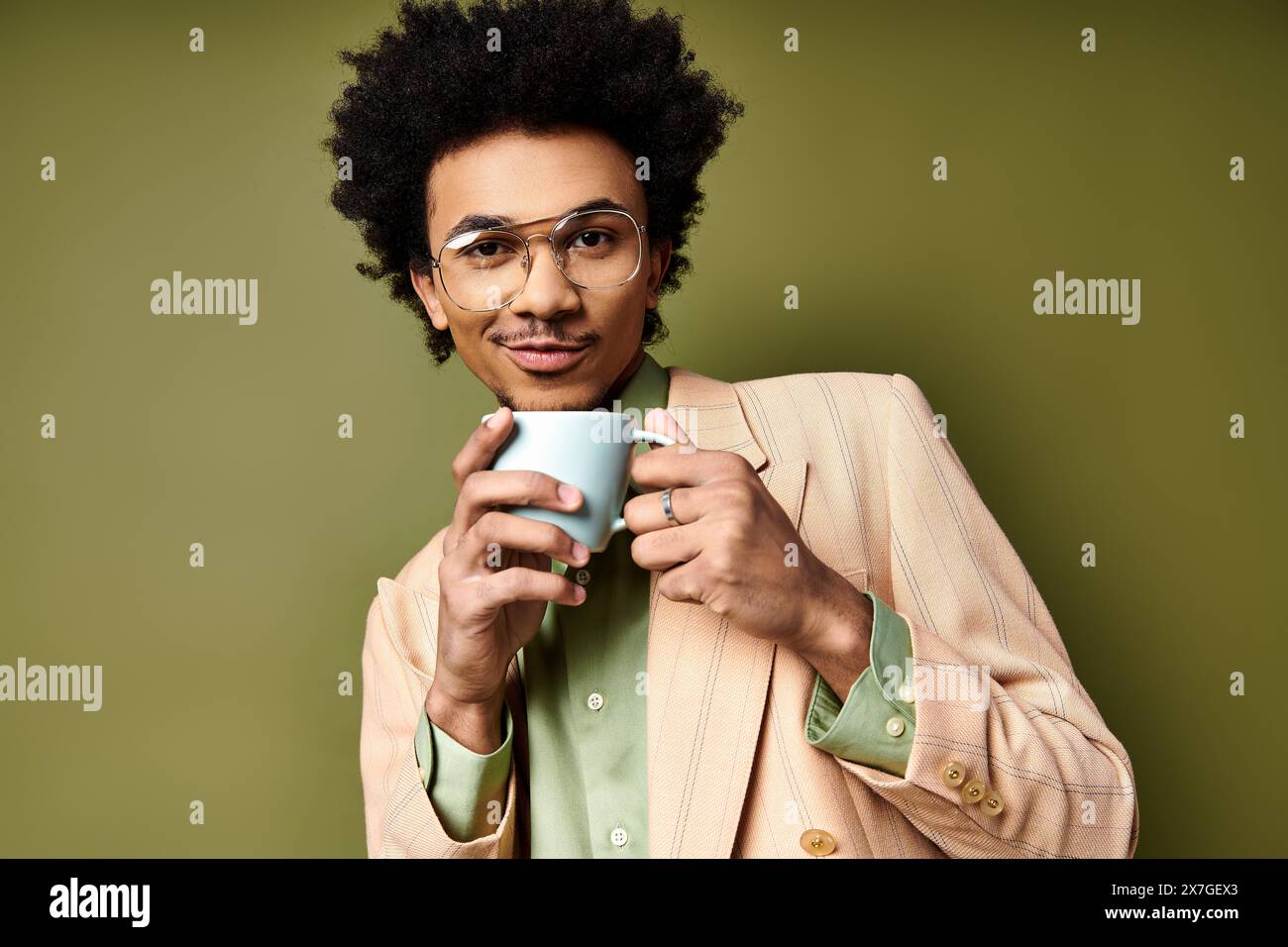 Un giovane afroamericano alla moda con capelli ricci e occhiali da sole regala una tazza di caffè fumante su uno sfondo verde. Foto Stock