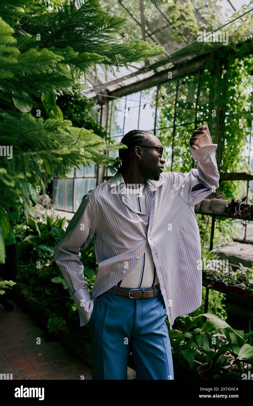Bell'uomo afroamericano in camicia bianca e pantaloni blu si posa nella lussureggiante serra. Foto Stock