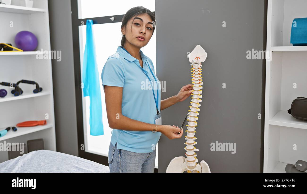 Una giovane terapeuta del sud asiatico in una clinica guida sulla salute della colonna vertebrale utilizzando un modello scheletrico. Foto Stock