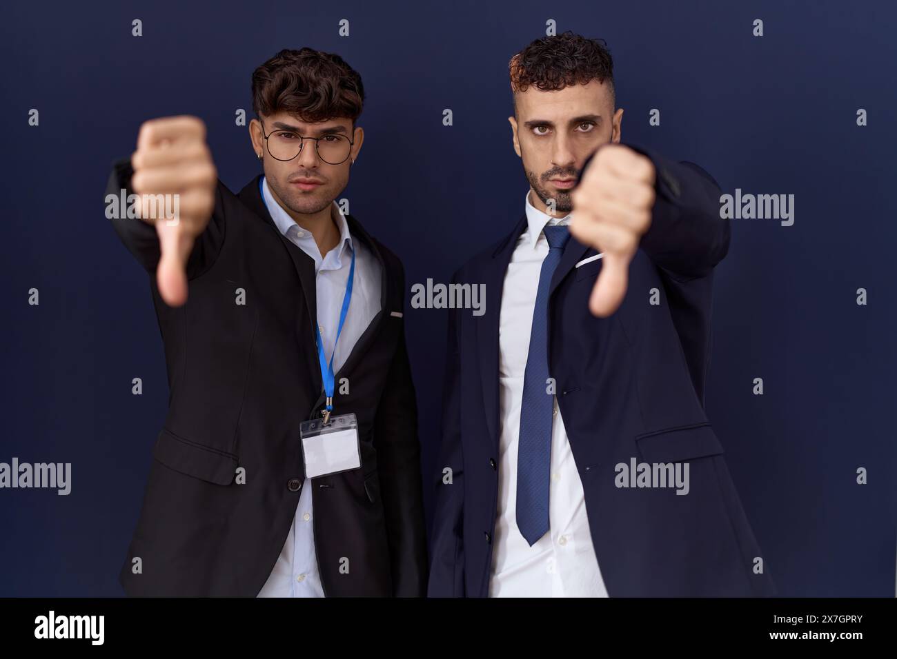 Due uomini d'affari ispanici che indossano abiti da lavoro sembrano infelici e arrabbiati mostrando rifiuto e negativo con il gesto dei pollici. espressione sbagliata. Foto Stock