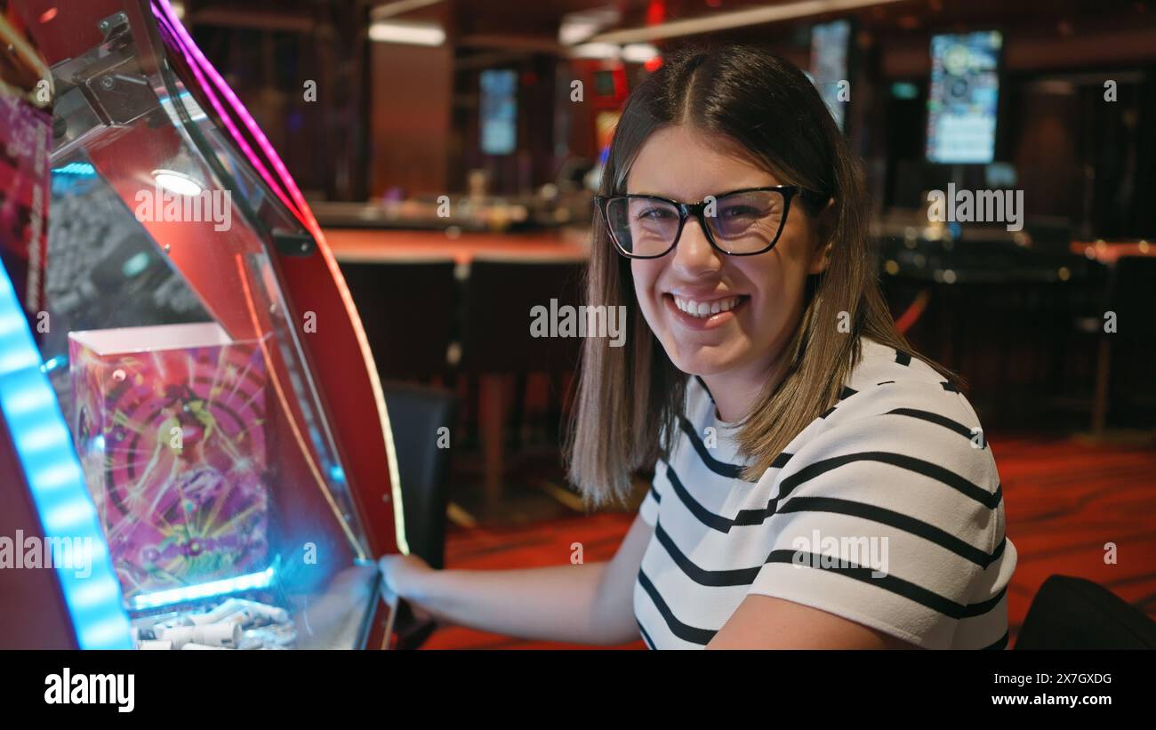 Una giovane allegra gioca a una slot machine in un vivace casinò, riflettendo il tempo libero e l'emozione. Foto Stock