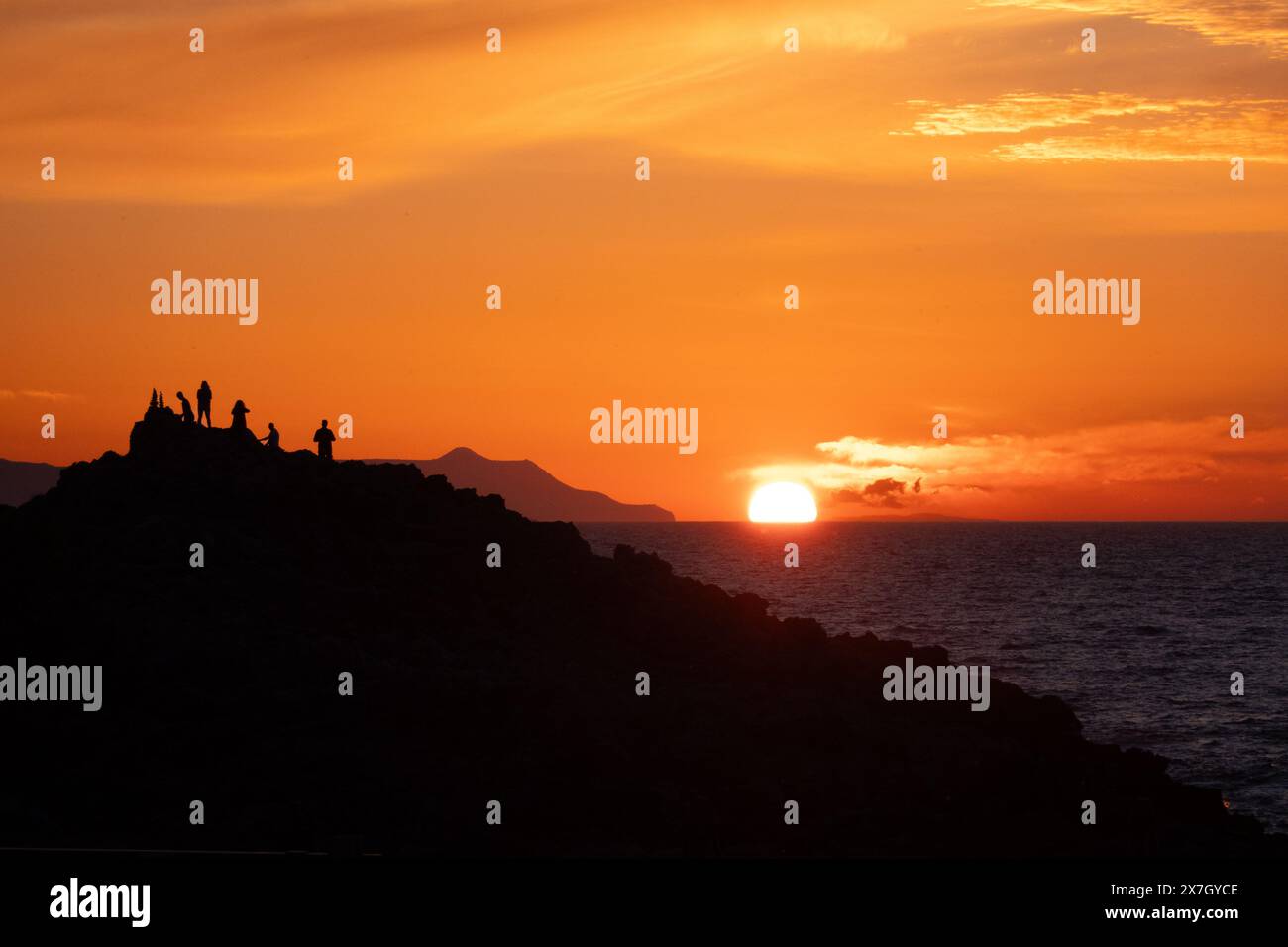 Sagoma di un gruppo di persone su una collina che guarda il tramonto sul mare Foto Stock