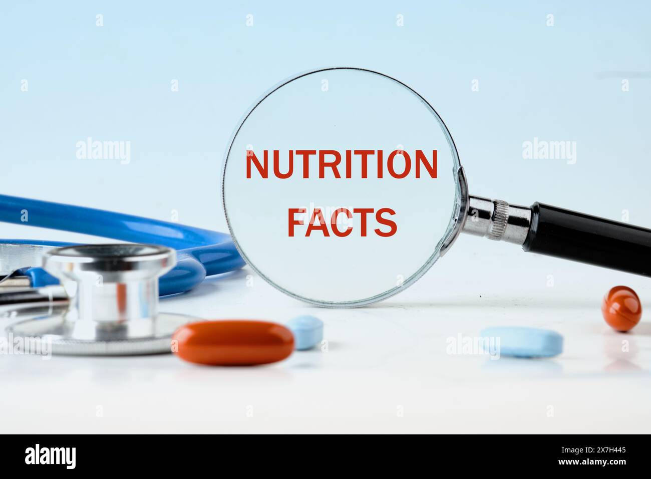 Un sacco di Nutrition Facts testo scritto attraverso una lente d'ingrandimento su uno sfondo azzurro, accanto alle pillole Foto Stock