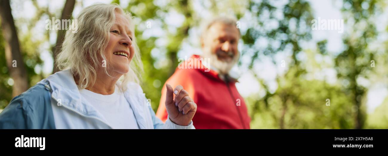 Concentrati su una donna anziana felice sorridente in abbigliamento sportivo che corre con l'uomo nel parco pubblico la mattina presto calda. Attività di jogging. Banner Foto Stock