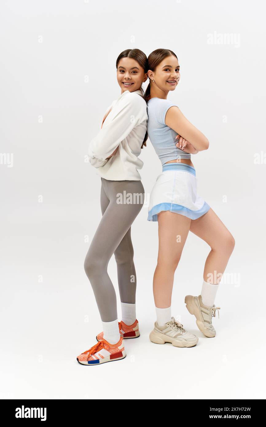 Due belle ragazze atletiche adolescenti, brune e abbigliamento sportivo, si stagliano fianco a fianco su uno sfondo grigio studio. Foto Stock