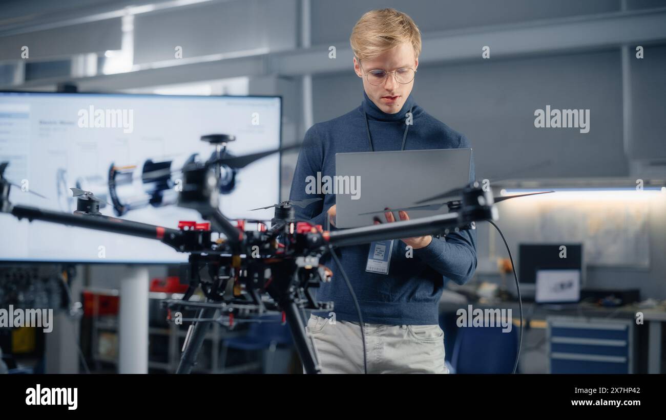 Young male Developer Programming on laptop computer. Lavorare su un nuovo progetto di droni nel laboratorio del centro di ricerca. Persone che creano un futuristico concetto di veicolo aereo senza pilota. Foto Stock