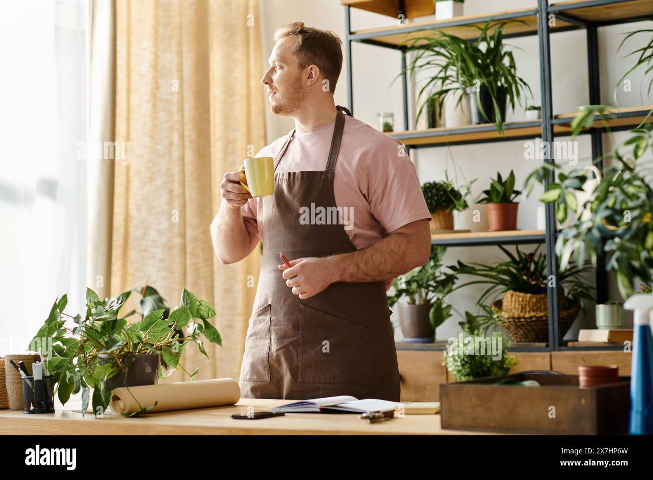 Un bell'uomo in un grembiule si gode una tazza di caffè in un negozio di piante, incarnando l'essenza di un piccolo imprenditore. Foto Stock