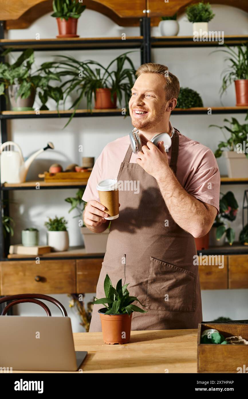 Un uomo in grembiule tiene una tazza di caffè in un negozio di piante, mostrando l'essenza di possedere una piccola impresa. Foto Stock