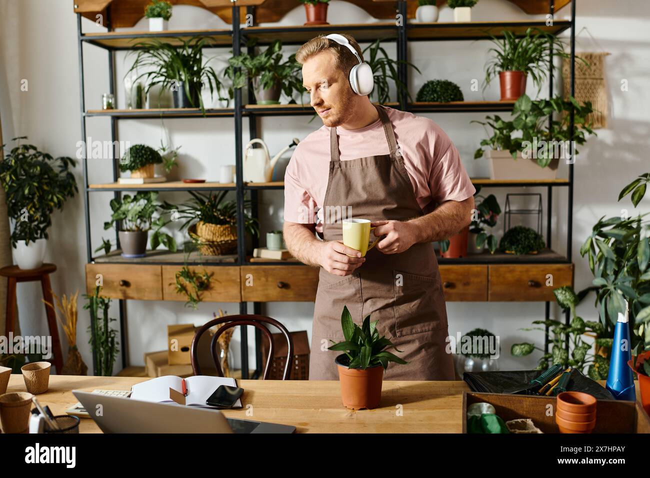 Un uomo in grembiule che si gusta una tazza di caffè in una fabbrica, mostrando il concetto di possedere una piccola impresa. Foto Stock