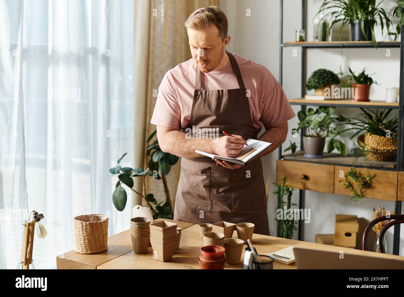 Un uomo in grembiule prende diligentemente appunti su un appunti in un negozio di piante, mostrando la sua dedizione alla sua piccola impresa. Foto Stock