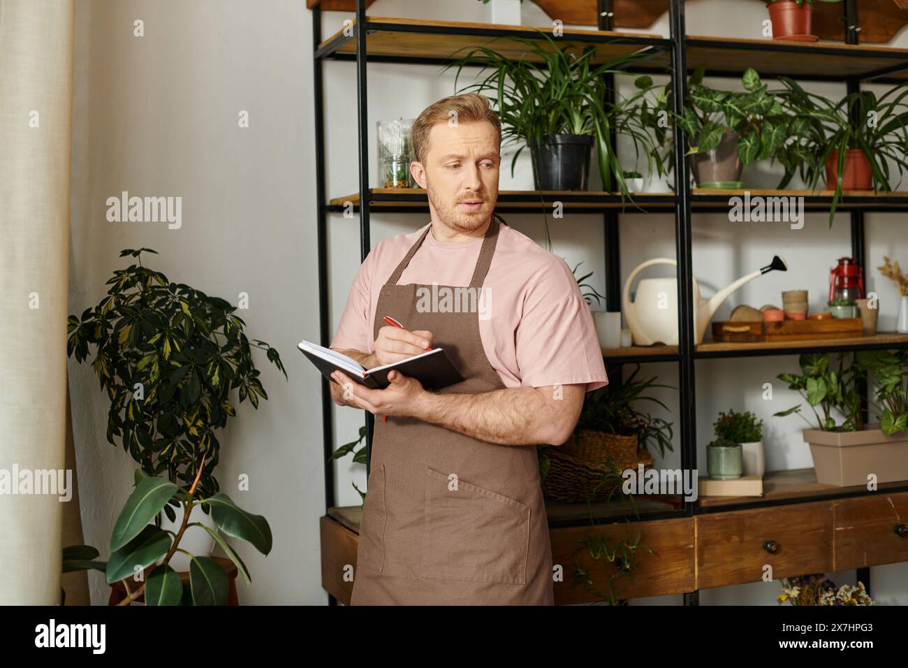 Un uomo carismatico in grembiule tiene con fiducia un appunti in un negozio di piante, incarnando lo spirito imprenditoriale e organizzativo. Foto Stock