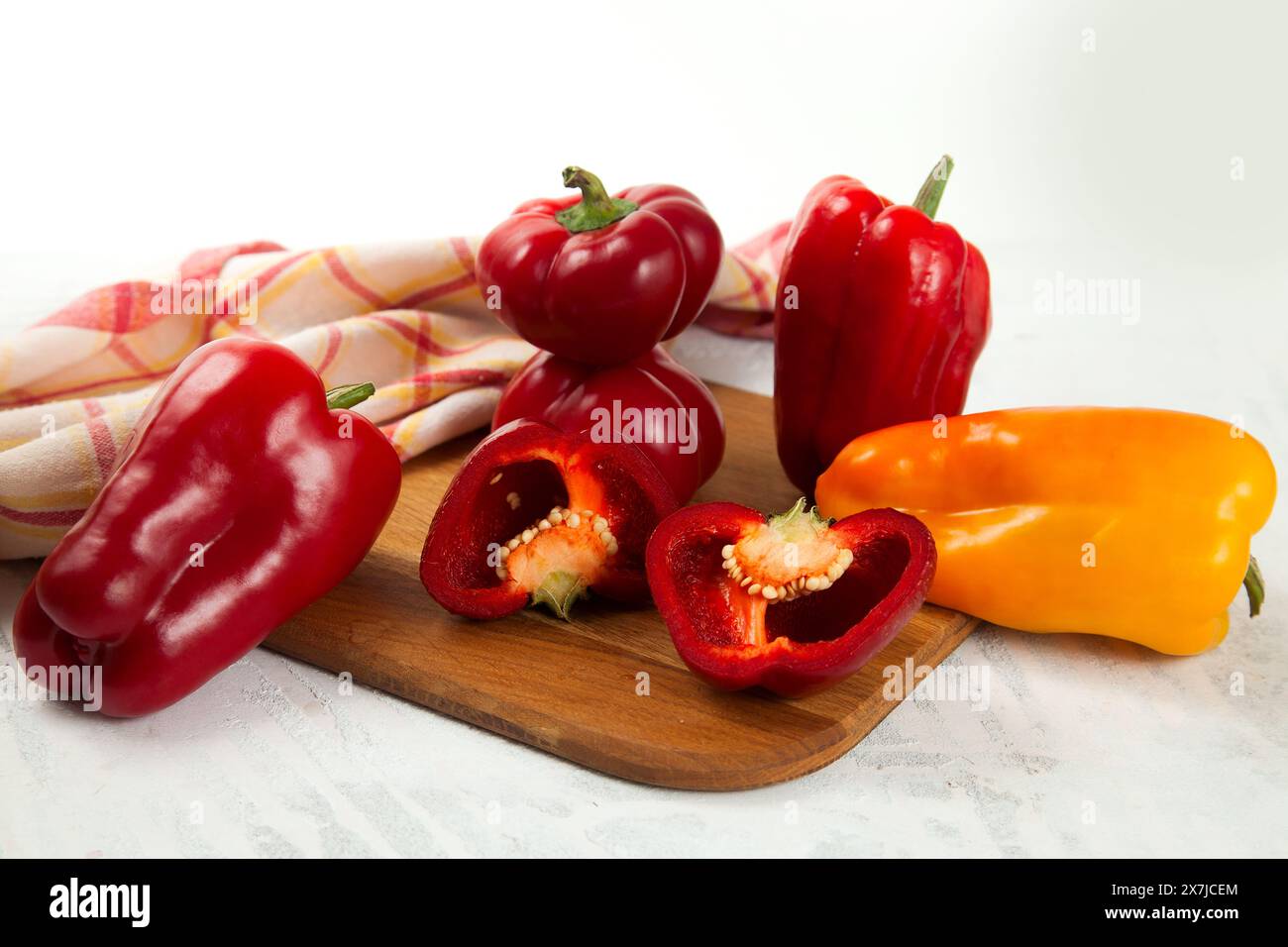 Tagliere con diverse tagliere interi e metà di peperoni rossi e gialli (capsicum) noti come peperoni dolci, paprika e asciugamano da cucina rosso su cui si trova Foto Stock