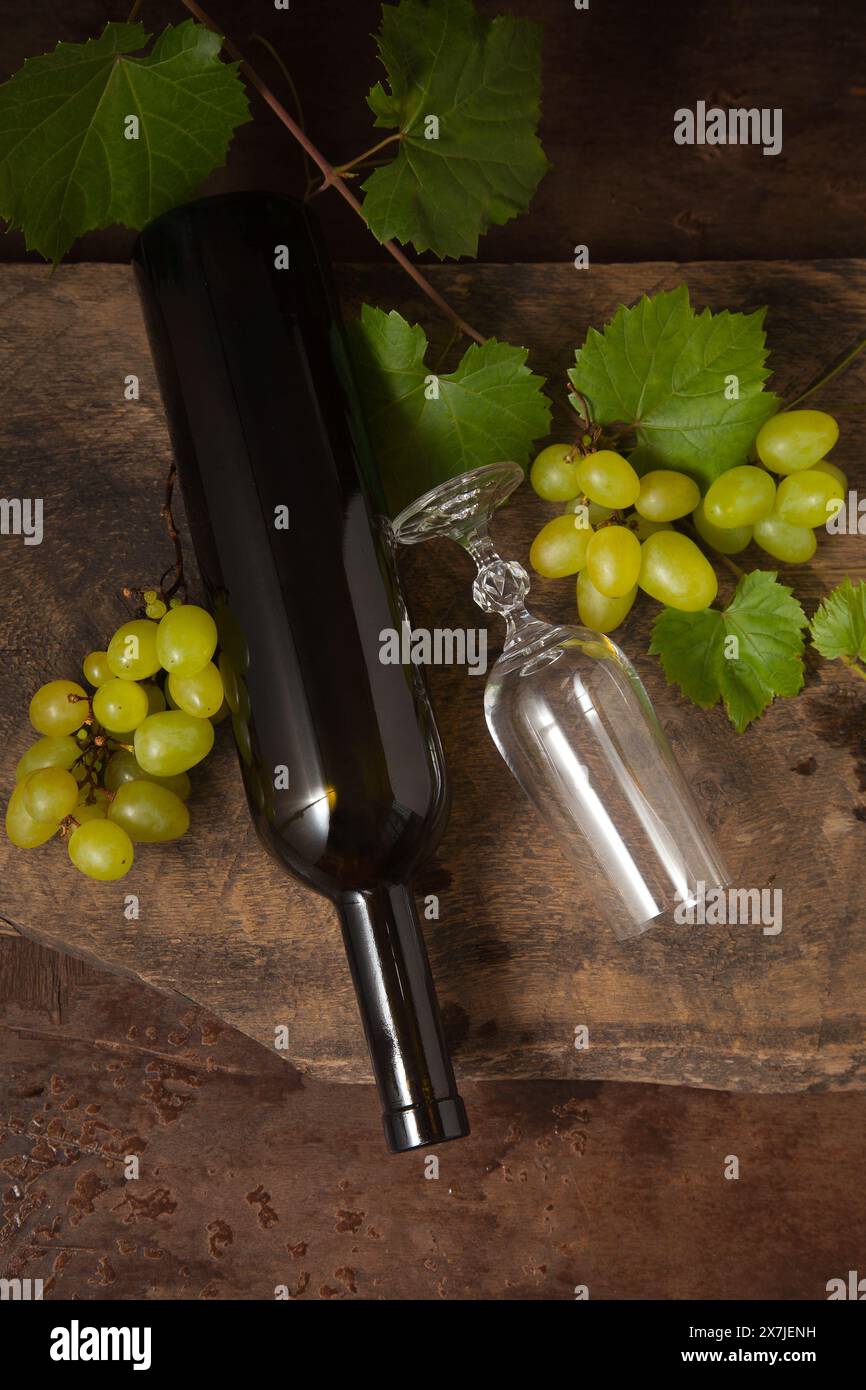Il concetto di una deliziosa bevanda alcolica, vino e uva. Vista dall'alto della bottiglia di vino, del bicchiere di vino vuoto e di un mazzo di uva su uno sfondo di legno rustico scuro Foto Stock