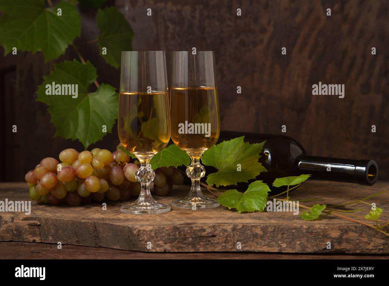 Il concetto di una deliziosa bevanda alcolica, vino e uva. Bottiglia di vino, due bicchieri di vino bianco e mazzo di uva rosa su bac in legno rustico scuro Foto Stock