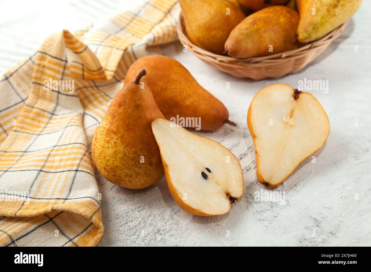 Diversi interi e metà di succosa frutta di pera matura, cesto di vimini con pere e asciugamano da cucina giallo su fondo di legno bianco. Foto Stock