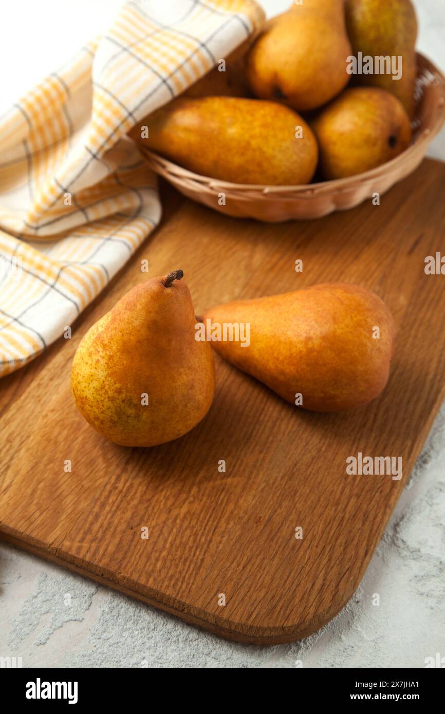 Tagliere in legno con frutta di pera matura e succosa, cesto di vimini con pere e asciugamano da cucina giallo su fondo di legno bianco. Foto Stock