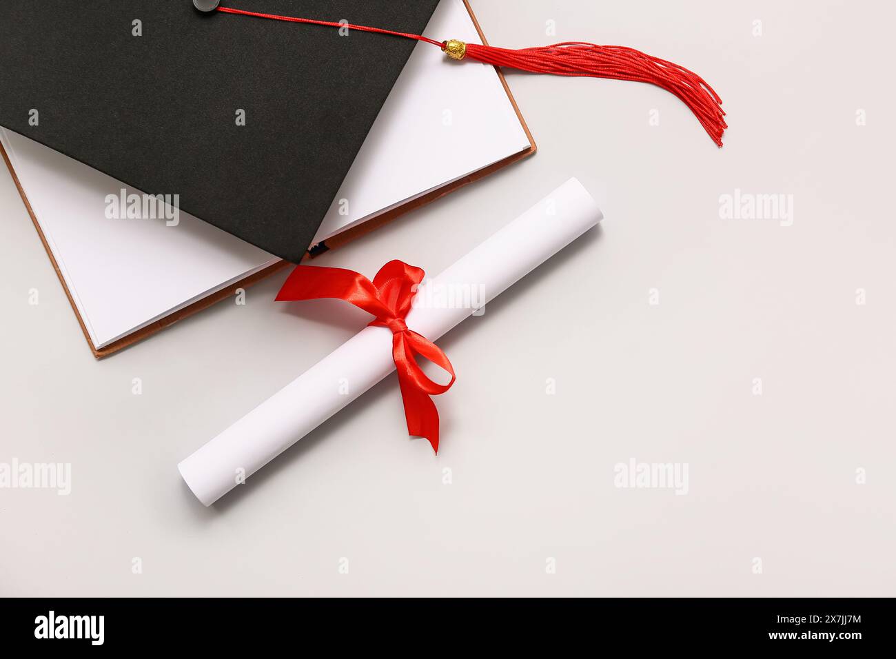Diploma con nastro rosso, libro aperto e cappello graduato su sfondo bianco Foto Stock