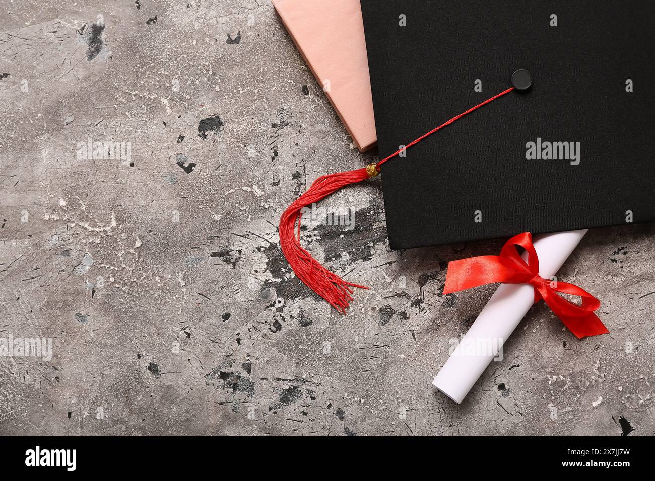 Diploma con nastro rosso, libro e cappello graduato su sfondo grunge grigio Foto Stock