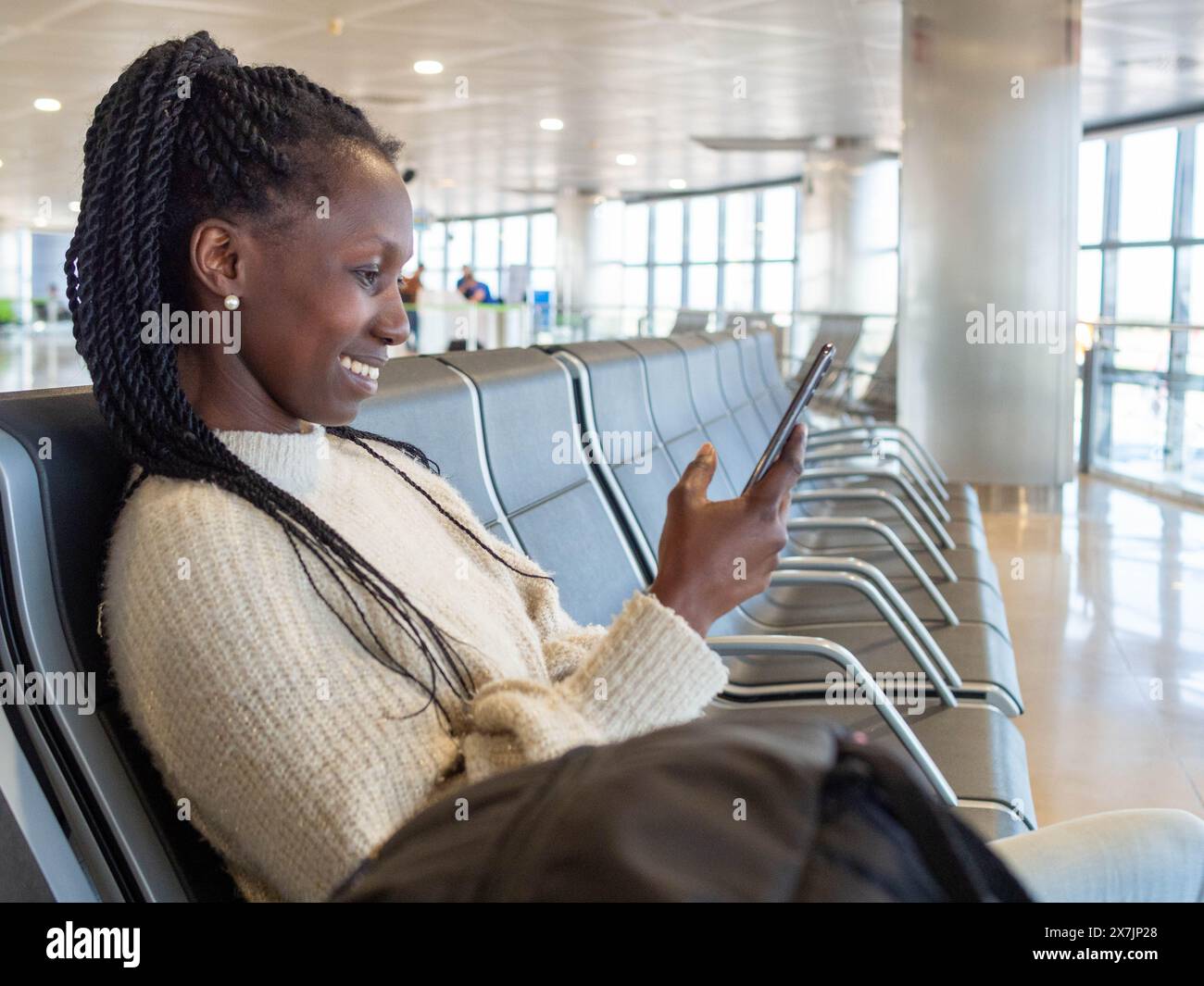 Una giovane donna che usa il suo telefono mentre aspetta il volo nella lounge dell'aeroporto Foto Stock