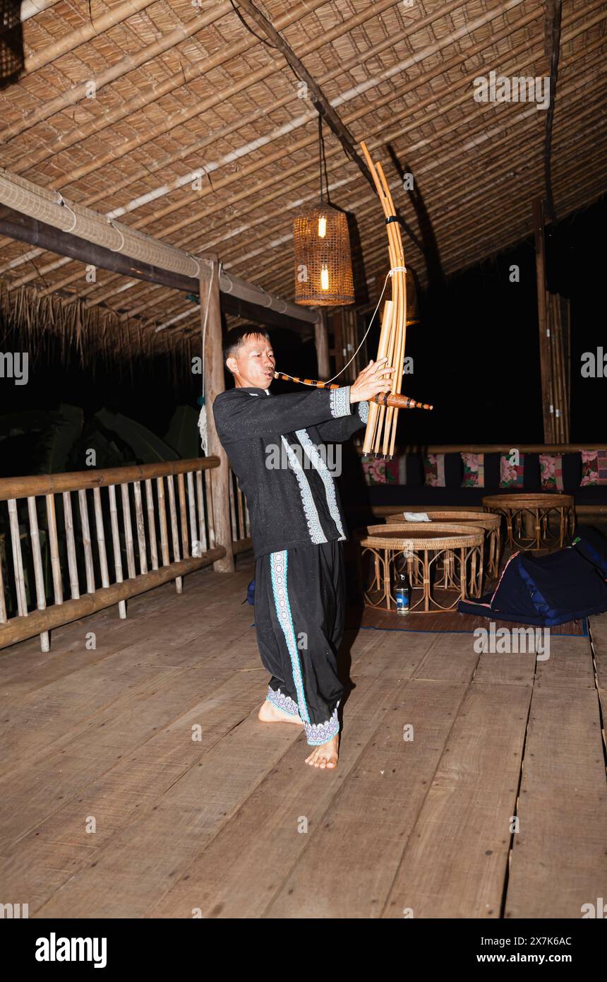 Un uomo hmong suona uno strumento musicale a Chiang Khong, nella provincia di Chiang Rai, nel nord della Thailandia, in colorato costume locale tradizionale Foto Stock