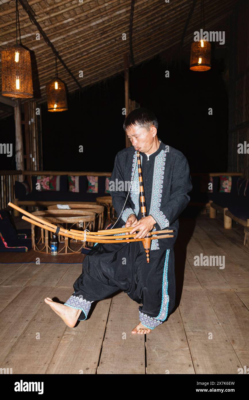 Un uomo hmong suona uno strumento musicale a Chiang Khong, nella provincia di Chiang Rai, nel nord della Thailandia, in colorato costume locale tradizionale Foto Stock