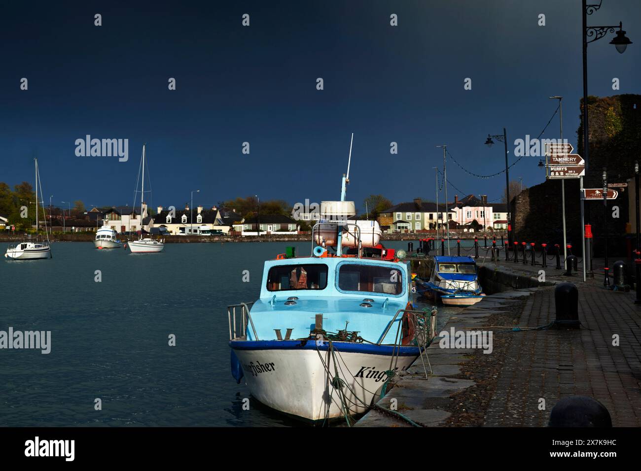 L'artigianato illuminato dal sole e le banchine si scontrano con le nuvole nere tempestose sopra Dungarvan Harbour nella contea di Waterford, Irlanda Foto Stock