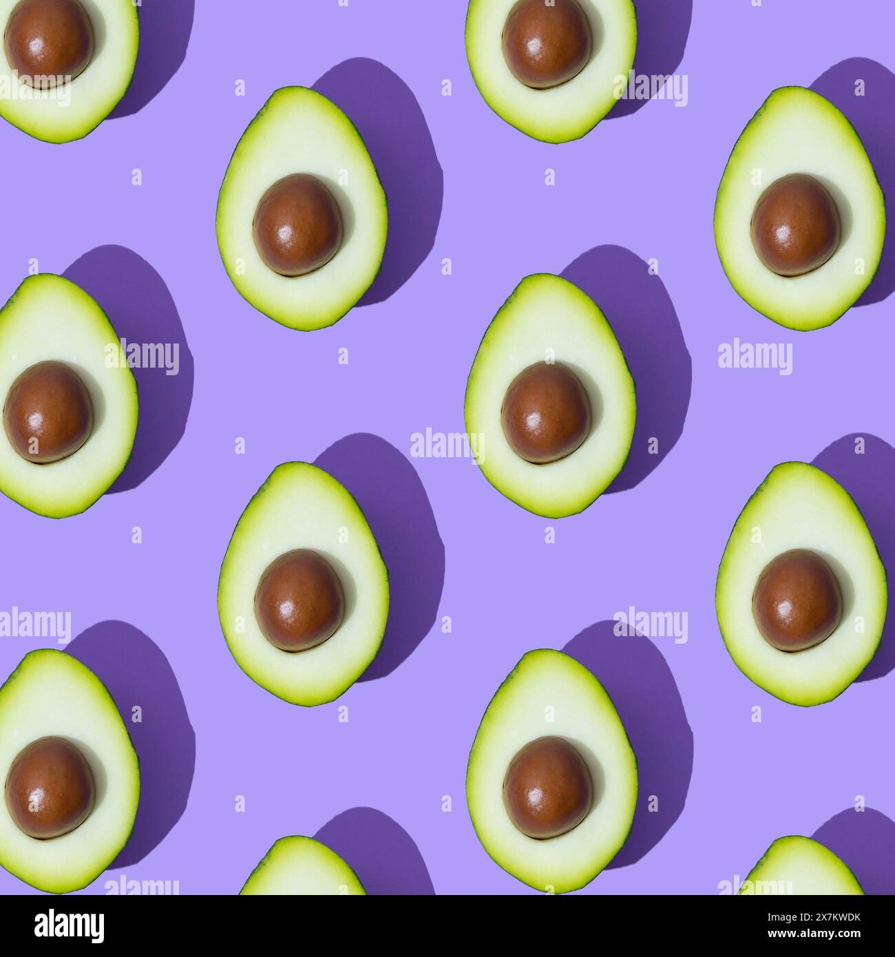 Motivo fresco avocado alla luce del sole su sfondo viola. Concetto di frutta biologica tropicale minimale. Dieta cruda o modello alimentare sano vegetariano. Foto Stock