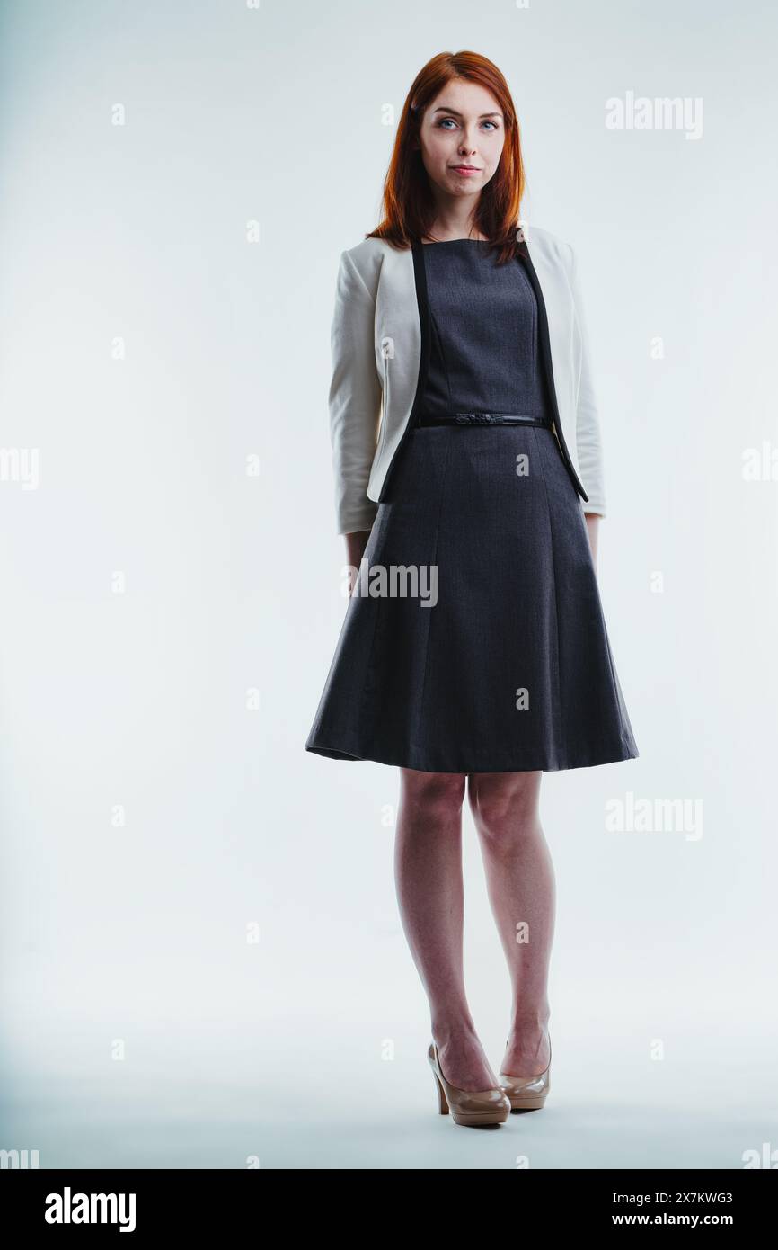 Sofisticata giovane donna con un abito scuro e un blazer grigio chiaro è pronta, il suo sguardo è stabile e sicuro Foto Stock