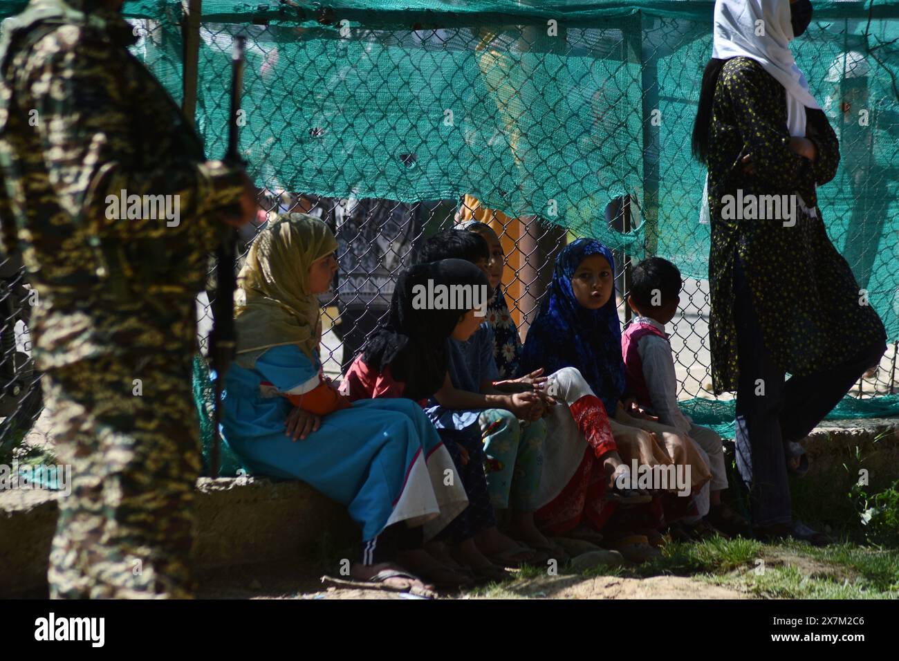 Baramulla, Jammu e Kashmir, India. 20 maggio 2024. Un soldato paramilitare si trova di guardia vicino ai bambini del Kashmir seduti all'interno di un seggio elettorale durante la quinta fase del voto alle elezioni generali in India, a nord del Kashmir il 20 maggio 2024. Le elezioni in India si svolgono in sette fasi nell'arco di sei settimane per alleviare l'immenso onere logistico di organizzare l'esercizio democratico nel paese più popoloso del mondo. (Credit Image: © Mubashir Hassan/Pacific Press via ZUMA Press Wire) SOLO PER USO EDITORIALE! Non per USO commerciale! Foto Stock